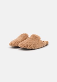 Tan schapenvacht instapslippers met een zachte, gestructureerde oppervlakte en een afgerond ontwerp. Voorzien van een low-profile houten zool.