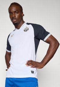 Tricou sport cu mânecă scurtă, având un corp alb și mâneci bleumarin, țesătură texturată și guler rotund. Include un logo și accente decorative.