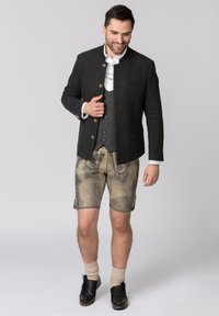 Traditionelles deutsches Outfit mit einer dunkelgrauen Wolljacke mit goldenen Knöpfen, grauem Weste, dekorativen beigen Lederhosen und schwarzen Schuhen.
