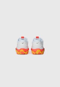 Des chaussures de sport blanches avec des accents rouges et jaunes, de forme arrondie, des semelles texturées et une languette à l'arrière pour un enfilage facile.