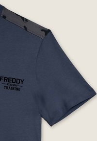 T-shirt blu navy con accenti in grigio mimetico sulle spalle, presenta un logo stampato nero "FREDDY ATHL DEPT TRAINING" sotto il colletto.