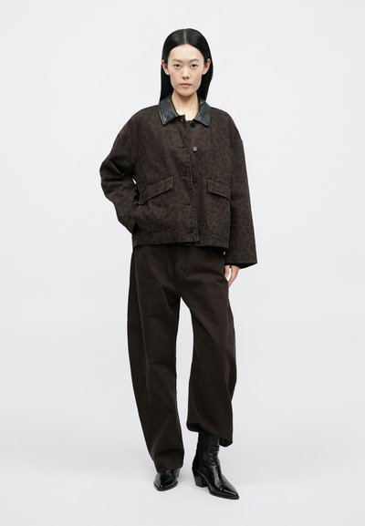 Casaco com estampa de leopardo castanho e gola de couro preta, combinado com calças castanhas largas e botas pretas até ao tornozelo. Fundo branco simples.