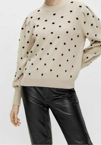 Beige sweater med sorte prikker, ribbede rund hals, og puffede lange ærmer, sammen med skinnende sorte læderbukser.
