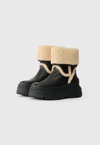 Μαύρες δερμάτινες μπότες έως τον αστράγαλο με χοντρή μαύρη πλατφόρμα, διαθέτοντας καφέ τεχνητό γούνινο τελείωμα και διακοσμητική υφή ραψίματος.