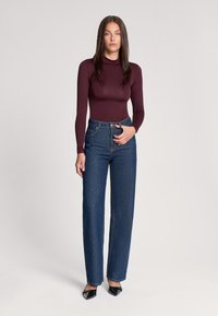 Burgundowy bodysuit z długim rękawem połączony z niebieskimi dżinsami o wysokim stanie. Dżinsy mają dwie przednie kieszenie i prosty krój nogawek. Czarne szpilki.