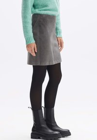 Grauer Cordrock mit strukturierter Oberfläche, kombiniert mit einem mintgrünen Pullover und schwarzen Ankle Boots, akzentuiert durch schwarze Strumpfhosen.