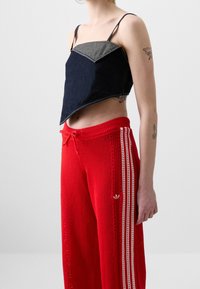 Denim crop-top, jossa on tumman sinisiä ja vaalean sinisiä paneeleja, ohutolkaimilla. Punaiset tekstuuri-housut valkoisilla sivuraitojen ja logotiedolla.