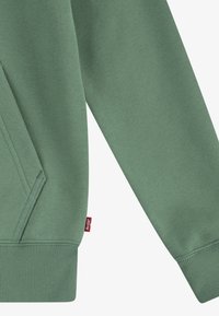 Felpa verde realizzata in morbido tessuto, con polsini e orlo a costine. Presenta una tasca a marsupio e un piccolo badge con logo sul lato.