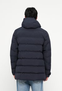 Navy puffer jacket with horizontal quilted pattern, high collar, and adjustable hood; features elastic cuffs and a relaxed fit.