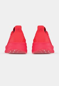 Chaussures de sport rouges vives avec une texture lisse et des semelles rembourrées, présentant un design profilé bas et un marquage en relief subtil sur les talons.