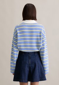 Jasnoniebieski sweter w zielone i białe paski, z białą prążkowaną kołnierzykiem. W zestawie z ciemnoniebieską spódnicą dżinsową o rozkloszowanym kroju.
