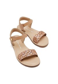 Sandalias marrones con correas ajustables en el tobillo y una tira trenzada de color cobre metálico a través de los dedos. Suela de goma plana, diseño minimalista.