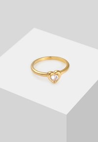Guldring med et hjerteformet design, prydet med en klar sten i midten. Glat, poleret overflade med en smal ring.