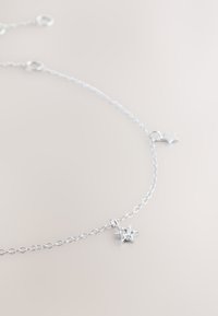 Delicate silver chain necklace with a small star-shaped pendant featuring a central clear stone on a light background.