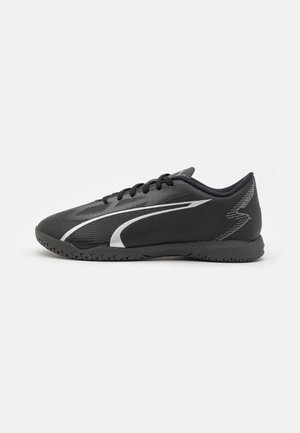 Czarne buty sportowe o gładkiej powierzchni, z eleganckim designem, zakrzywionymi białymi akcentami oraz gumową podeszwą z wzorzystą przyczepnością.