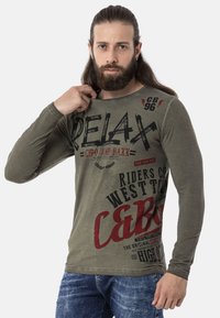 Langärmliges olivgrünes Hemd mit fettem Text und Grafiken in Schwarz und Rot, mit rundem Ausschnitt und weichem Material.