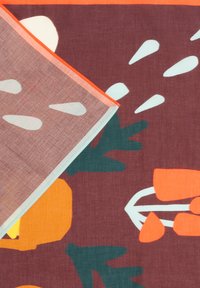 Tela marrón con formas abstractas en naranja, blanco y verde oscuro que parecen plantas y hojas, con una esquina doblada que muestra el lado reverso.