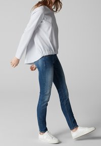 Světle modrý pruhovaný dlouhý rukáv s vykrojeným lemem v kombinaci s přiléhavými tmavými džíny a bílými teniskami; ležérní oufit s jednoduchými akcenty.