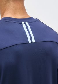 Άνω μέρος της πλάτης ενός ατόμου που φοράει μπλε ναυτικό πουκάμισο με δύο κάθετες ανοιχτό μπλε ρίγες κοντά στη λαιμόκοψη.