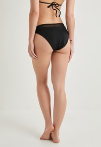 Parte inferior de bikini negra con un diseño de cintura alta, que presenta detalles de material transparente en la parte superior y una textura suave.