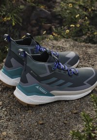 Graue und türkisfarbene Wanderschuhe mit einer strukturierten Oberseite, blauen Schnürsenkeln und einer auffälligen weißen Zwischensohle. Verfügt über konsistente geometrische Akzente und Markenkennzeichnung.