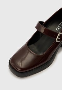 Chaussure Mary Jane en cuir verni bordeaux avec un bout carré, une sangle réglable, et une semelle plateforme noire texturée.