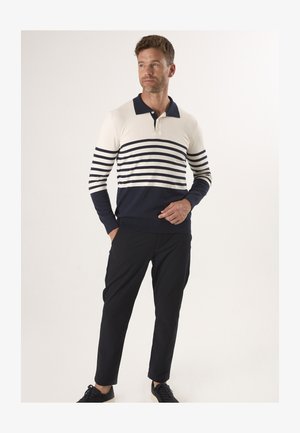 Polo rayé bleu marine et crème à manches longues avec col et patte de boutonnage à trois boutons ; associé à un pantalon noir tapered et des baskets foncées.