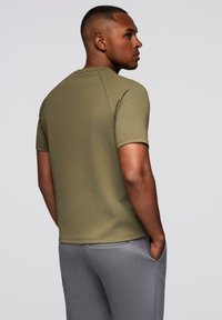 Olivengrøn T-shirt med korte ærmer, rund hals og raglanærmer, parret med grå bukser. Glat tekstur, afslappet pasform.