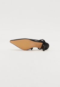 Escarpin noir à talon aigu avec un talon fin et courbé. Présente un extérieur lisse et une semelle marron clair, accentuée par un logo.
