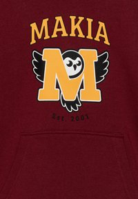 Bordo dukserica s kapuljačom koja sadrži veliki žuti logotip "M" s crtanom sovom i krilima, a iznad je tekst "MAKIA", osnovano 2001.