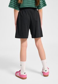 Svarta shorts med elastisk midja, kombinerade med rosa sneakers och vita strumpor. Toppen är grön med svarta horisontella ränder.
