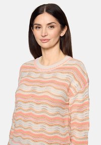 Pull en maille avec un motif ondulé en rose, pêche et beige, présentant une texture en maille ouverte et un col rond.