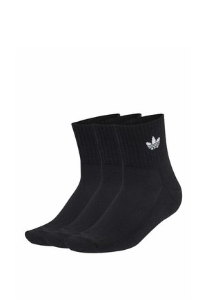 Trzy czarne skarpety za kostkę z prążkowanymi ściągaczami i białym logo Adidas trefoil na kostce, ułożone obok siebie na białym tle.