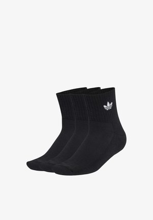 Tre calze nere da ginnastica con polsini a coste e logo Adidas trefoil bianco sulla caviglia, disposte affiancate su sfondo bianco.