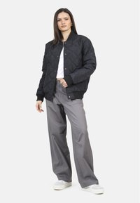 Zwarte gewatteerde bomberjack met ruitpatroon, geribbelde boorden en kraag. Gecombineerd met lichtgrijze wijde broek en witte sneakers.