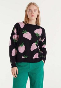 Suéter negro con patrones de fresas rosas y hojas verdes. Mangas largas, escote redondo. Combinado con pantalones de pana verdes.