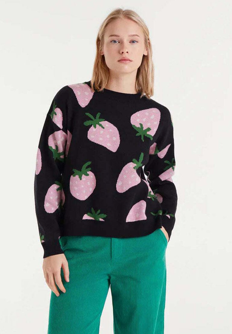Suéter negro con patrones de fresas rosas y hojas verdes. Mangas largas, escote redondo. Combinado con pantalones de pana verdes.