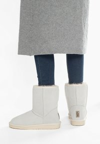 Botines de ante gris con un suave forro de piel de fur y suela de goma marrón, con un patrón cosido y una etiqueta de marca en el talón.