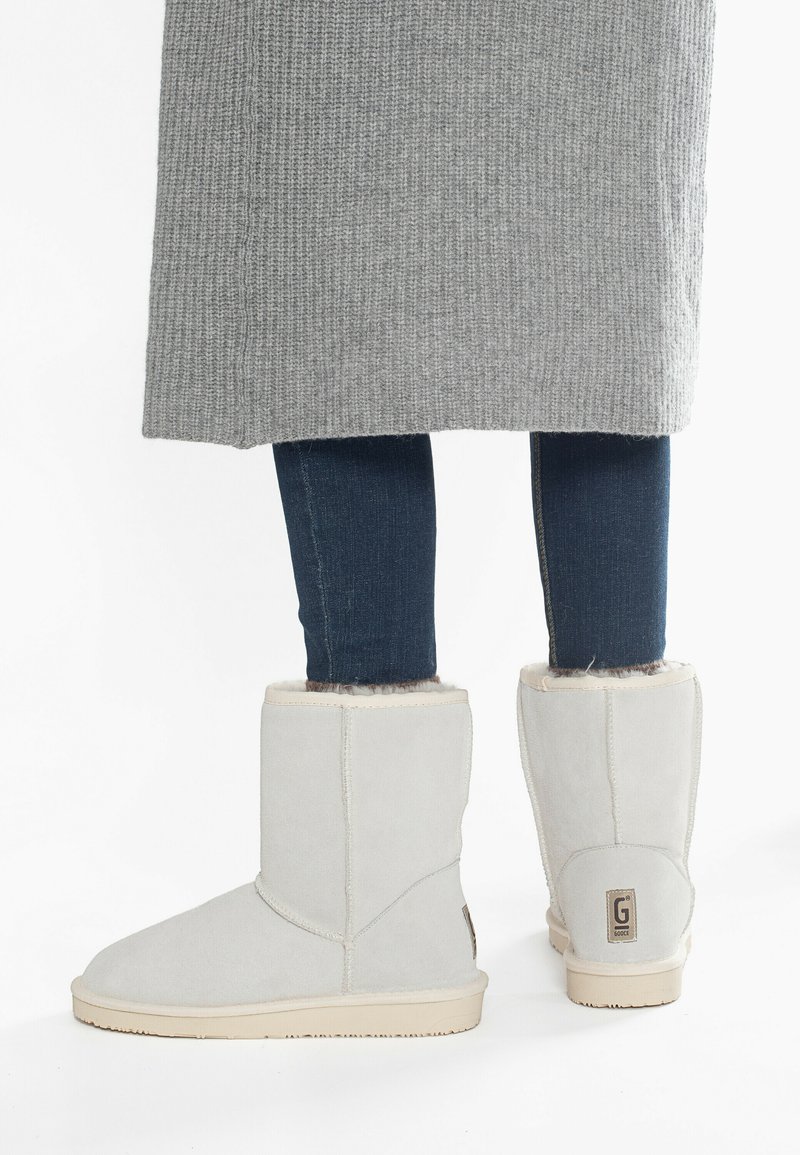Botines de ante gris con un suave forro de piel de fur y suela de goma marrón, con un patrón cosido y una etiqueta de marca en el talón.