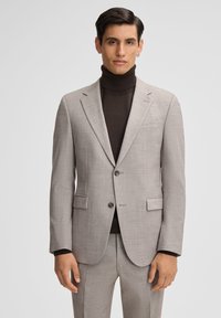 Hellgrauer Blazer aus strukturiertem Stoff, mit aufgesetzten Revers und zwei Knöpfen, getragen über einem dunklen Rollkragenpullover. Vordertaschen sichtbar.