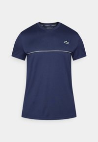 Granatowy T-shirt z krótkim rękawem i okrągłym dekoltem, ozdobiony białym poziomym paskiem oraz zielonym logo krokodyla na lewej piersi.