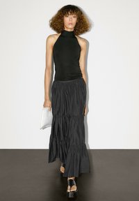 Top senza maniche nero con collo alto abbinato a una gonna lunga nera a strati, realizzata in un tessuto testurizzato e scarpe con tacco a piattaforma nere eleganti.