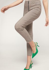 Högt midjebyxor med rutmönster i beige, brunt och svart, kombinerat med ljusgröna slingback-skorn. Slät yta med dragkedjedetalj.