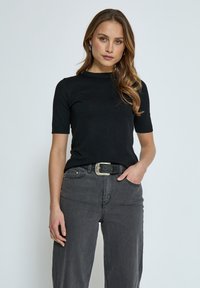 Top corto de punto negro con cuello redondo, combinado con jeans oscuros de tiro alto y un cinturón con hebilla plateada. Textura suave.