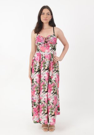Femme posant dans une robe maxi sans manches à fleurs roses et blanches avec de fines bretelles et des sandales beiges à bout ouvert.
