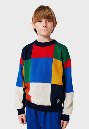 Colorful knitted sweater featuring a geometric patchwork design with red, blue, green, yellow, and beige sections; ribbed neckline and cuffs.