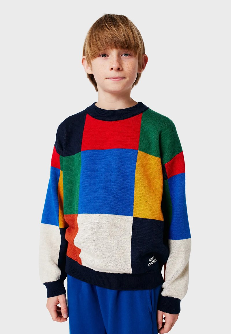 Suéter de punto colorido con un diseño de patchwork geométrico que incluye secciones en rojo, azul, verde, amarillo y beige; con cuello y puños acanalados.