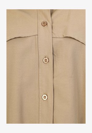 Beige Knopfhemd mit weicher Textur, ausgestattet mit einem spitzen Kragen, zwei Brusttaschen und braunen Knöpfen. Einfaches und neutrales Design.