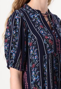 Navy dress featuring floral embroidery in blue and pink, vertical stripes, short puff sleeves, and a keyhole neckline with ties.