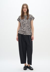 Top a maniche corte con motivo zebra in beige e nero; abbinato a pantaloni neri larghi e scarpe nere. Taglio semplice e tessuto leggero.